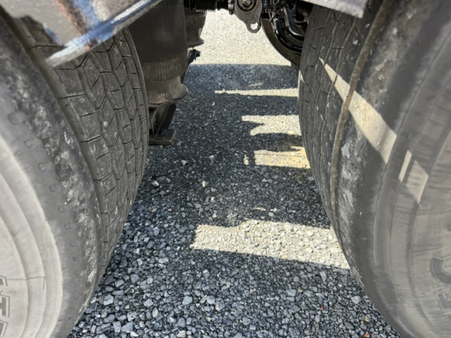 Volvo VNL64T300 truck undercarriage showing rear dual tires and gap between axles. Visible tread and gravel surface.