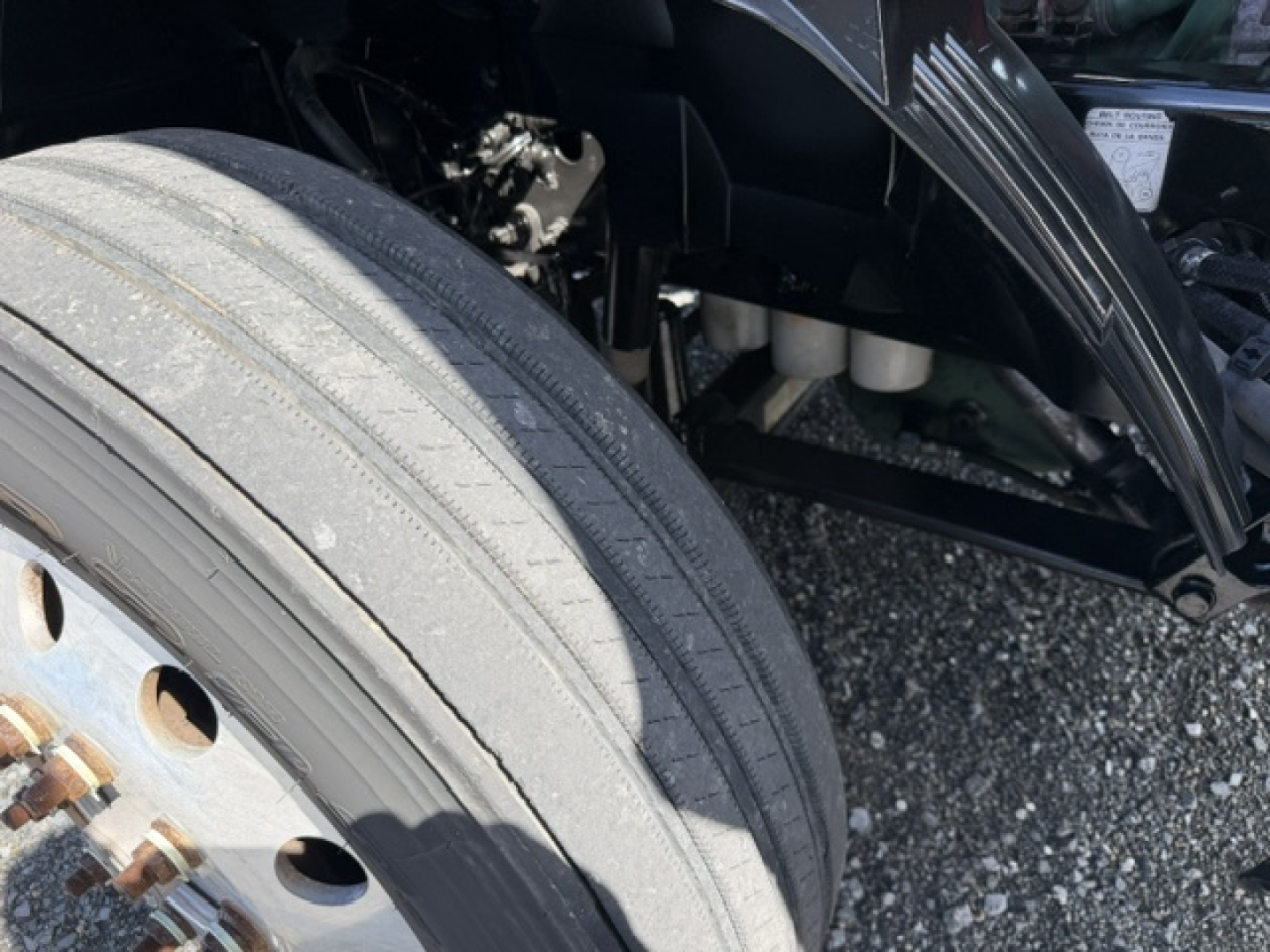 Truck wheel and front suspension area of a 2016 Volvo VNL64T300 showing tire tread and wheel hub, with engine bay components visible in background.