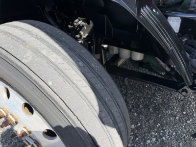 Truck wheel and front suspension area of a 2016 Volvo VNL64T300 showing tire tread and wheel hub, with engine bay components visible in background.