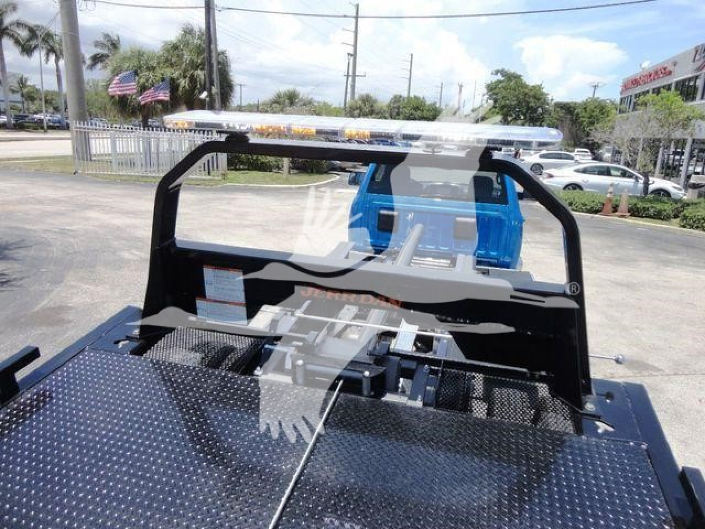Ram 5500 rollback truck bed with black diamond plate deck and blue cab in background. View shows loading area and rear frame with tie-downs and canopy frame.