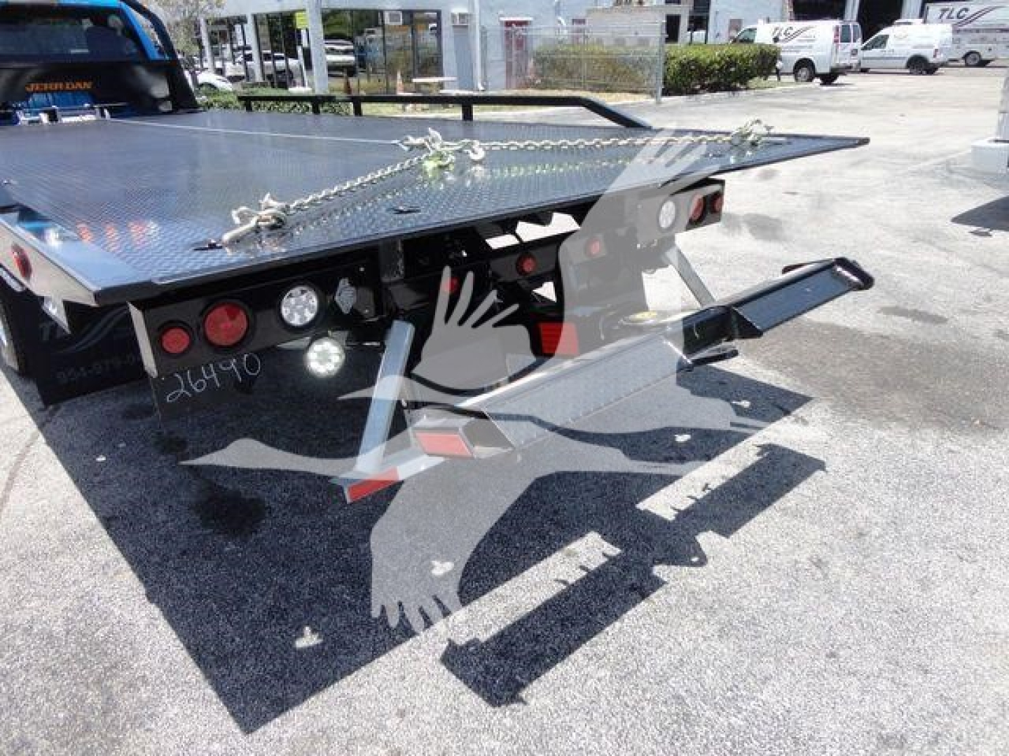 Ram 5500 rollback truck flatbed with chain tie-downs and ramps; rear view showing metal flatbed and towing hitch area.