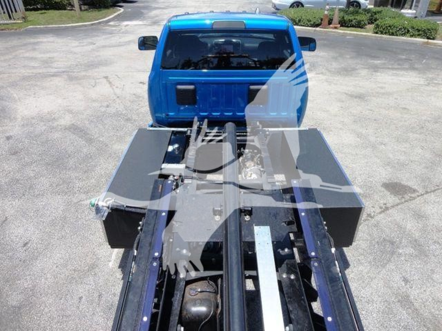 Ram 5500 rollback truck bed showing chassis and hydraulic components with blue cab in background.