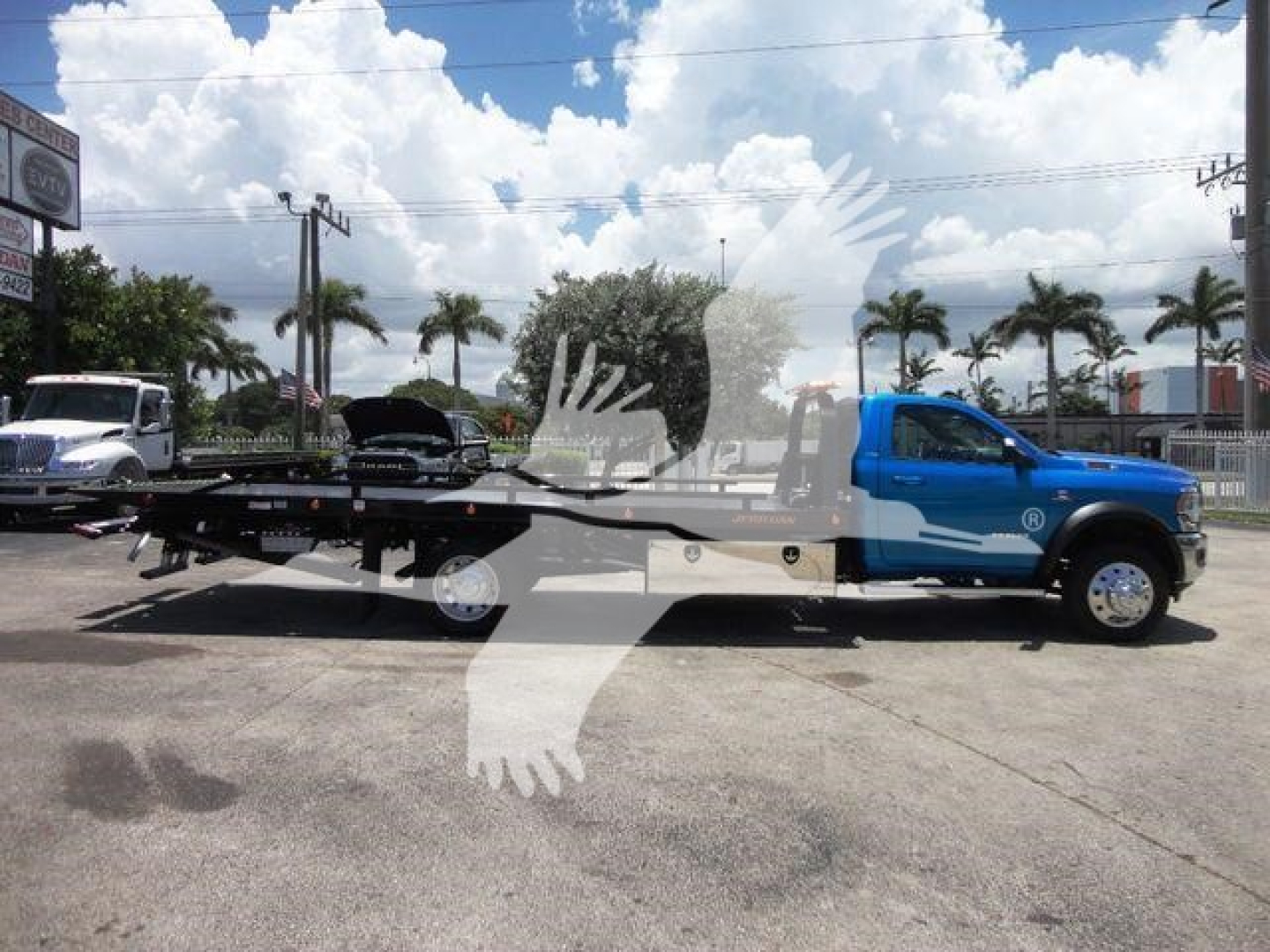 Ram 5500 rollback truck side view showing blue cab and long black flatbed with wheel lift in a dealership lot.