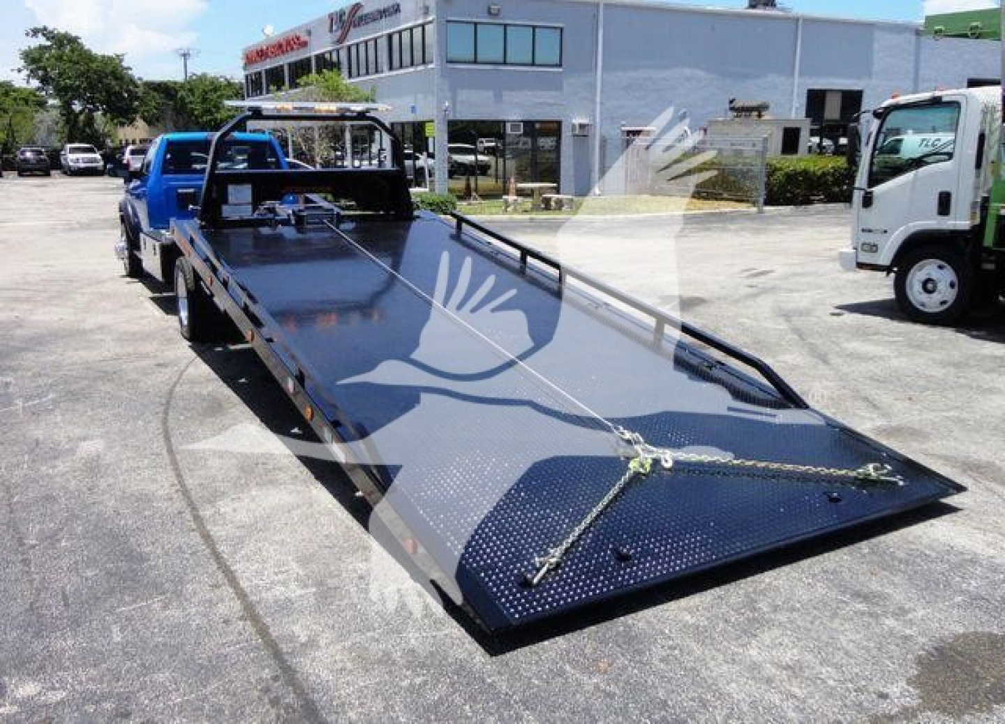 Ram 5500 rollback flatbed truck in-service showing a long black metal platform with ramp edges and tie-down chains.