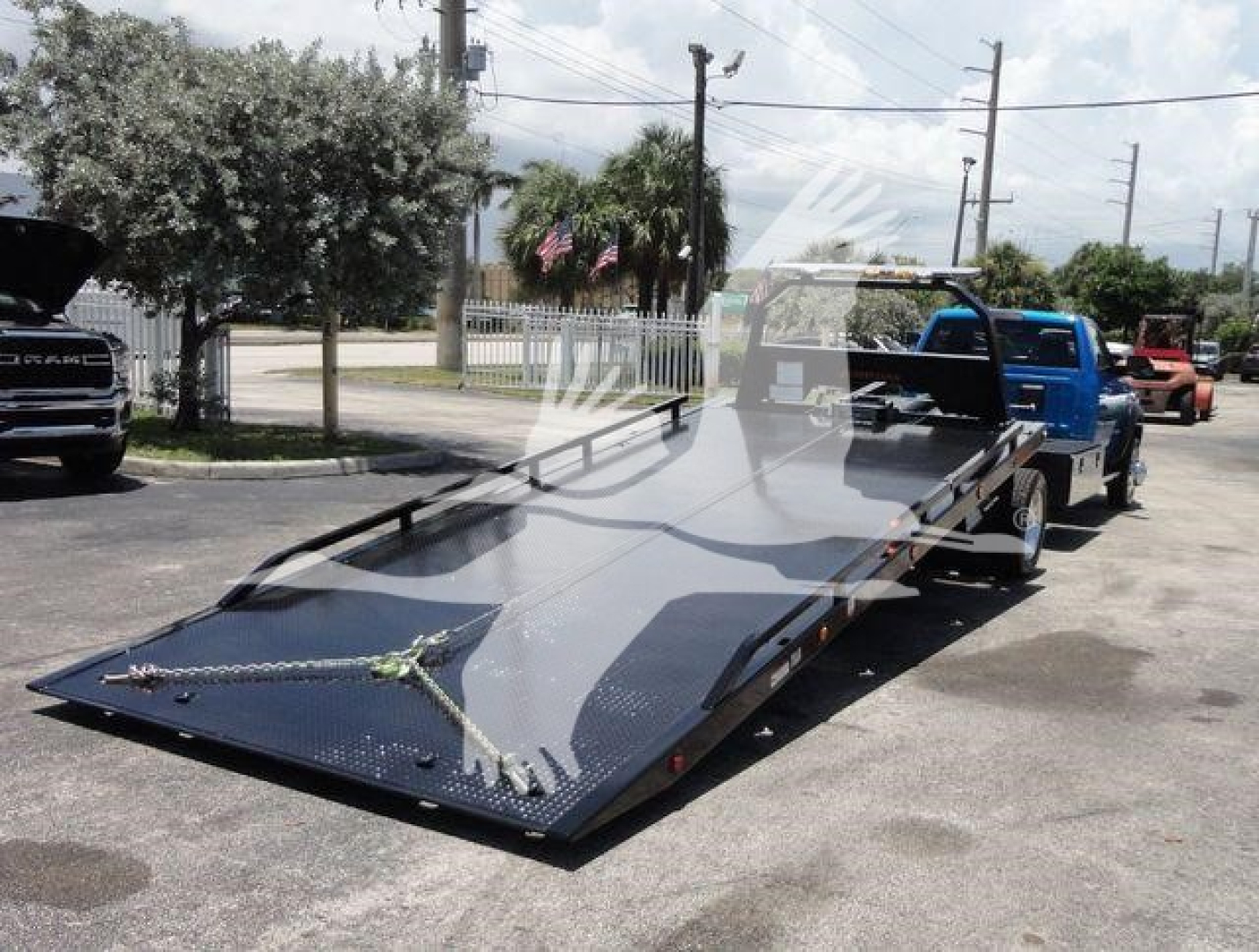 Ram 5500 SLT flatbed rollback tow truck with blue cab and extended flatbed in a parking lot.