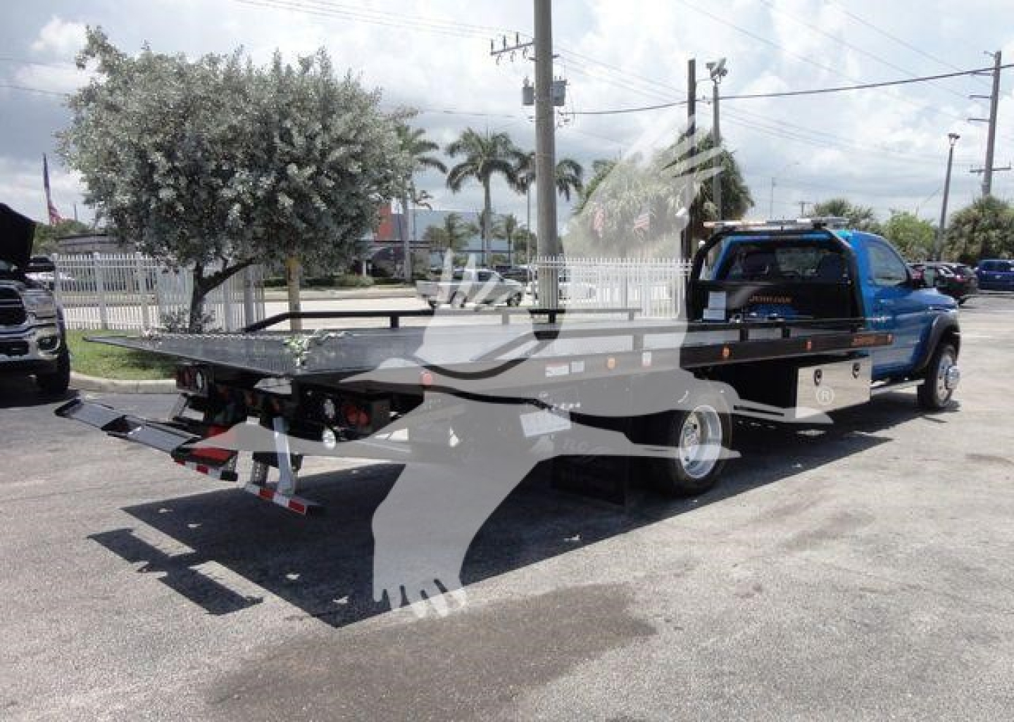 Ram 5500 SLT pickup truck with rollback bed showing flatbed and ramps in a dealership lot.