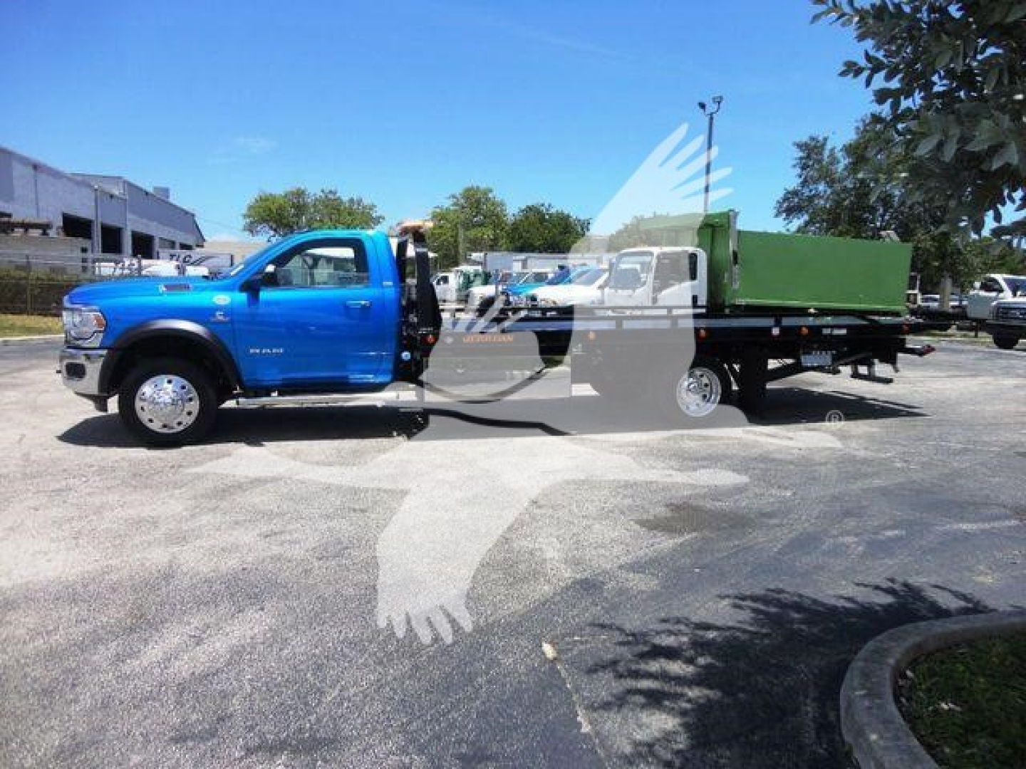 Blue Ram 5500 truck in rollback configuration showing cab and flatbed with green dumpster attachment, side profile view.