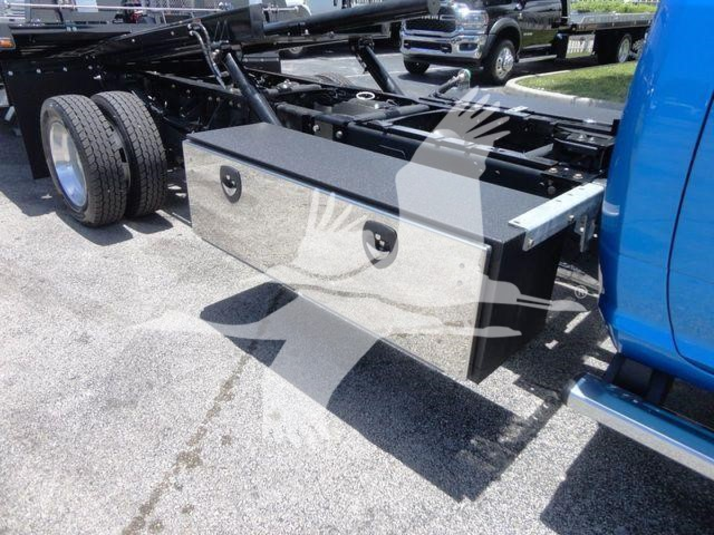 Truck chassis with a rectangular metal storage box mounted behind the cab on a blue Ram 5500 rollback. Storage box has two recessed handles and a black top.
