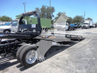 Truck bed tow rig chassis in 2024 Ram 5500 SLT showing rollback equipment and front wheel; image includes other trucks in background.