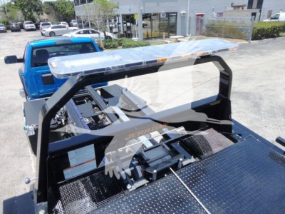 Ram 5500 rollback tow truck with blue cab and aluminum flatbed viewed from rear/side showing winch and hydraulic components.