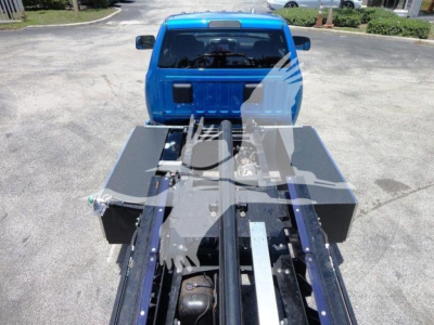 Ram 5500 rollback truck bed showing chassis and hydraulic components with blue cab in background.