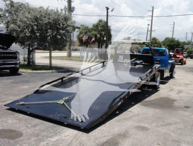Ram 5500 SLT flatbed rollback tow truck with blue cab and extended flatbed in a parking lot.