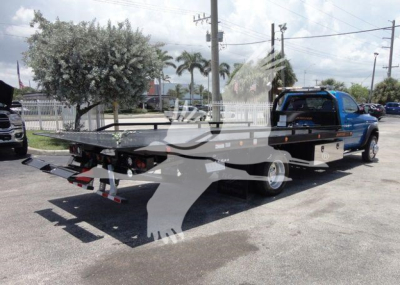Ram 5500 SLT pickup truck with rollback bed showing flatbed and ramps in a dealership lot.
