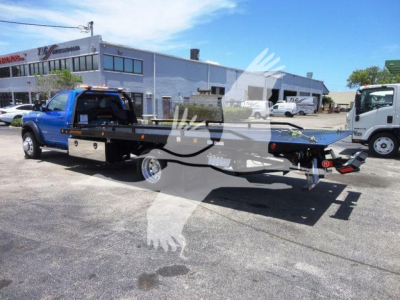 Ram 5500 SLT rollback truck bed shown in blue pickup with flatbed tow setup and trailer hitch, in dealership lot with other trucks in background.
