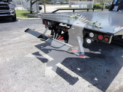 Rear view of a new Ram 5500 SLT rollback truck body with diamond plate platform, taillights, and jacking ramps visible.