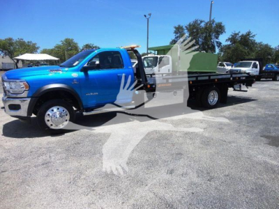 Ram 5500 truck with blue cab and rollback flatbed, side view showing extended cab and dual rear wheels.