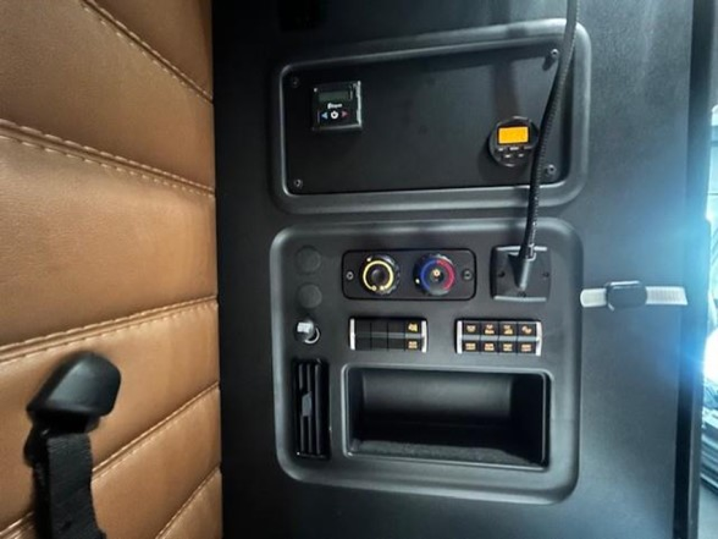 Trucking cab interior showing dashboard controls and vertical seat with brown upholstery in a Freightliner Cascadia sleeper.