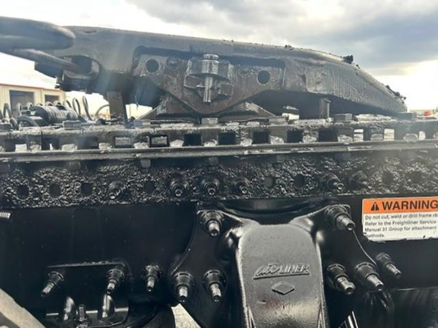 Truck engine bay showing Freightliner cascadia components with visible bolts and a brand stamp on a metal plate.