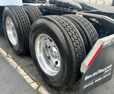 Freightliner Cascadia 126 rear axle area with dual rear tires and chrome rims. Visible text on mudflap: 'TRUCKS SELECTI...  (800) 999-2512' and tire sidewall marks.