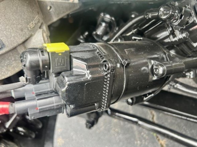 Engine bay showcasing a compact electrical/air module with a yellow-tipped connector and multiple wiring harnesses in a Freightliner Cascadia engine compartment.