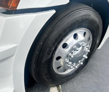 Freightliner Cascadia front wheel showing tire and polished steel rim with lug nuts.