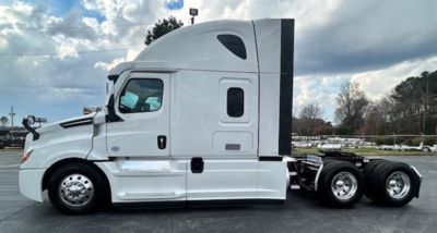 Truck side view showing Freightliner Cascadia sleeper cab with white paint, fuel tanks, and rear tandem wheels.