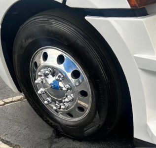 Truck wheel and tire on a Freightliner Cascadia; polished chrome hub with lug nuts; tire sidewall shows brand/model text partially; front fender and bumper nearby.