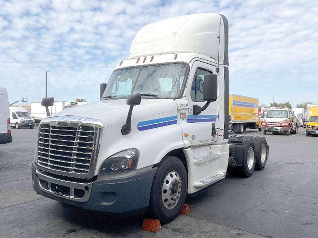 Truck cab showing Freightliner Evolution Cascadia 125 sleeper with white cab, blue stripe, and attached trailer in a lot.
