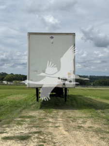 Trailer rear view showing a Utility 4000D-X box trailer with a small emblem and latch visible; no legible model text due to distance.