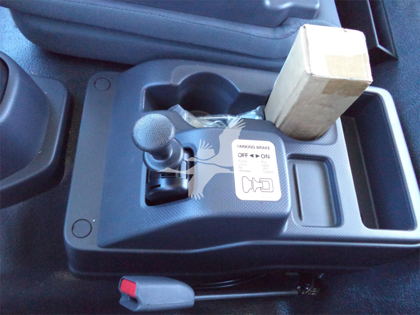 Isuzu FTR interior center console showing parking brake lever, gear shift shifter, cup holder, and a small cardboard box placed in the storage compartment.