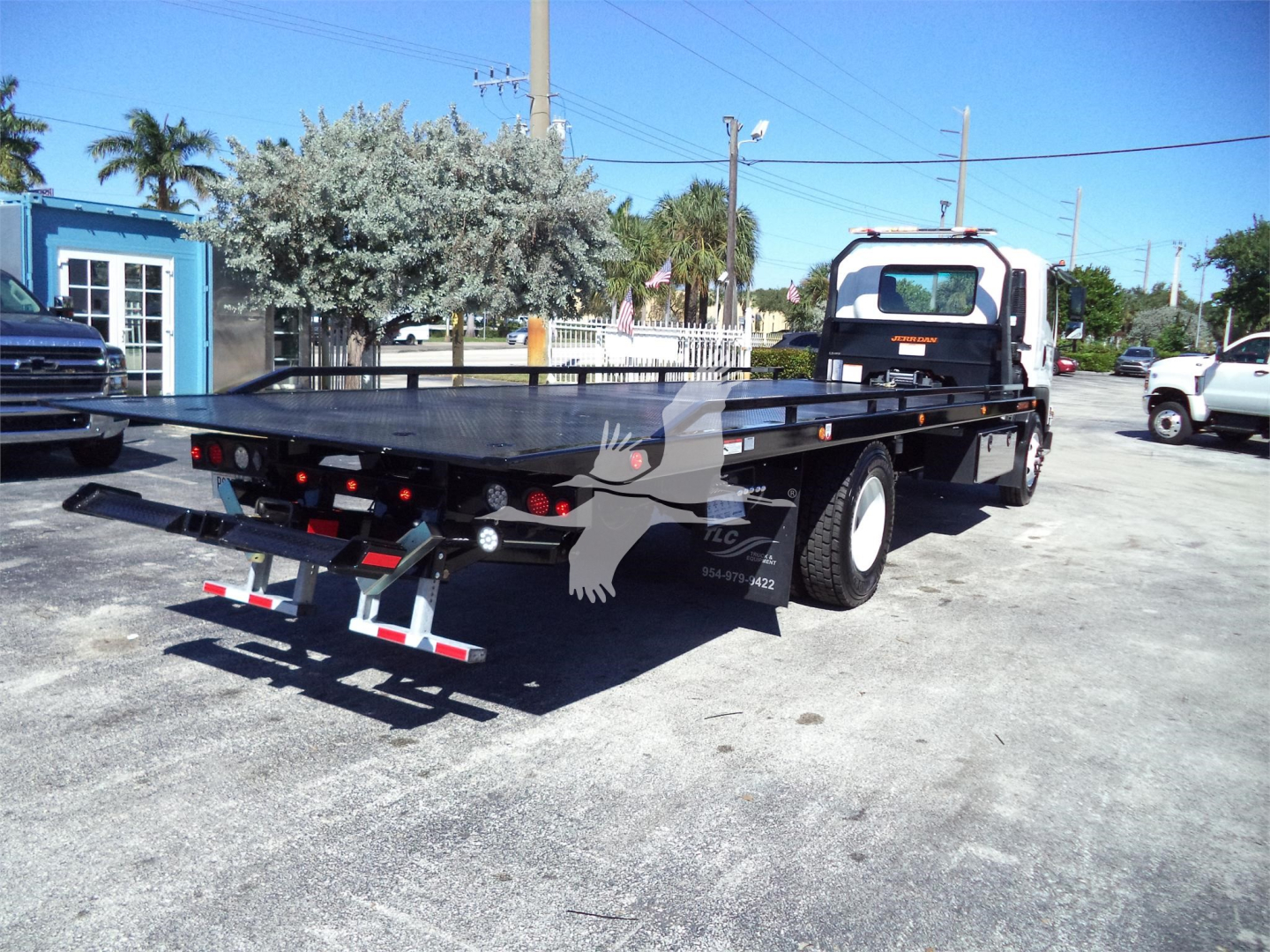 Isuzu rollback tow truck with flatbed trailer in a parking lot, rear view showing flatbed and taillights.