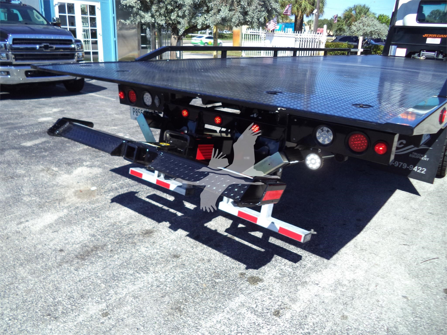Isuzu FTR rollback bed showing hydraulic wheel lift and bumper accessories; flatbed with diamond plate surface and taillights visible.