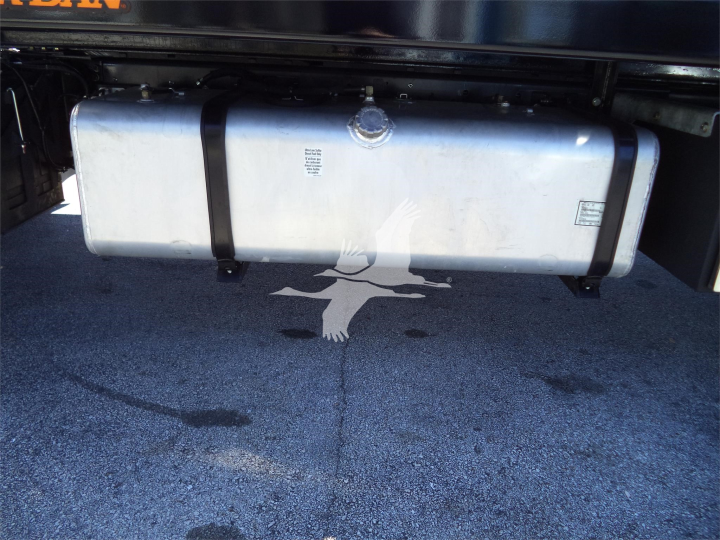 Isuzu FTR rollback truck fuel tank and undercarriage with two side straps and a central cap, visible on a paved surface.