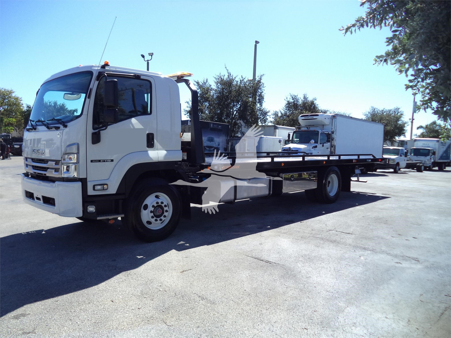 Isuzu FTR rollback tow truck side view showing flatbed with hydraulic equipment and white cab.