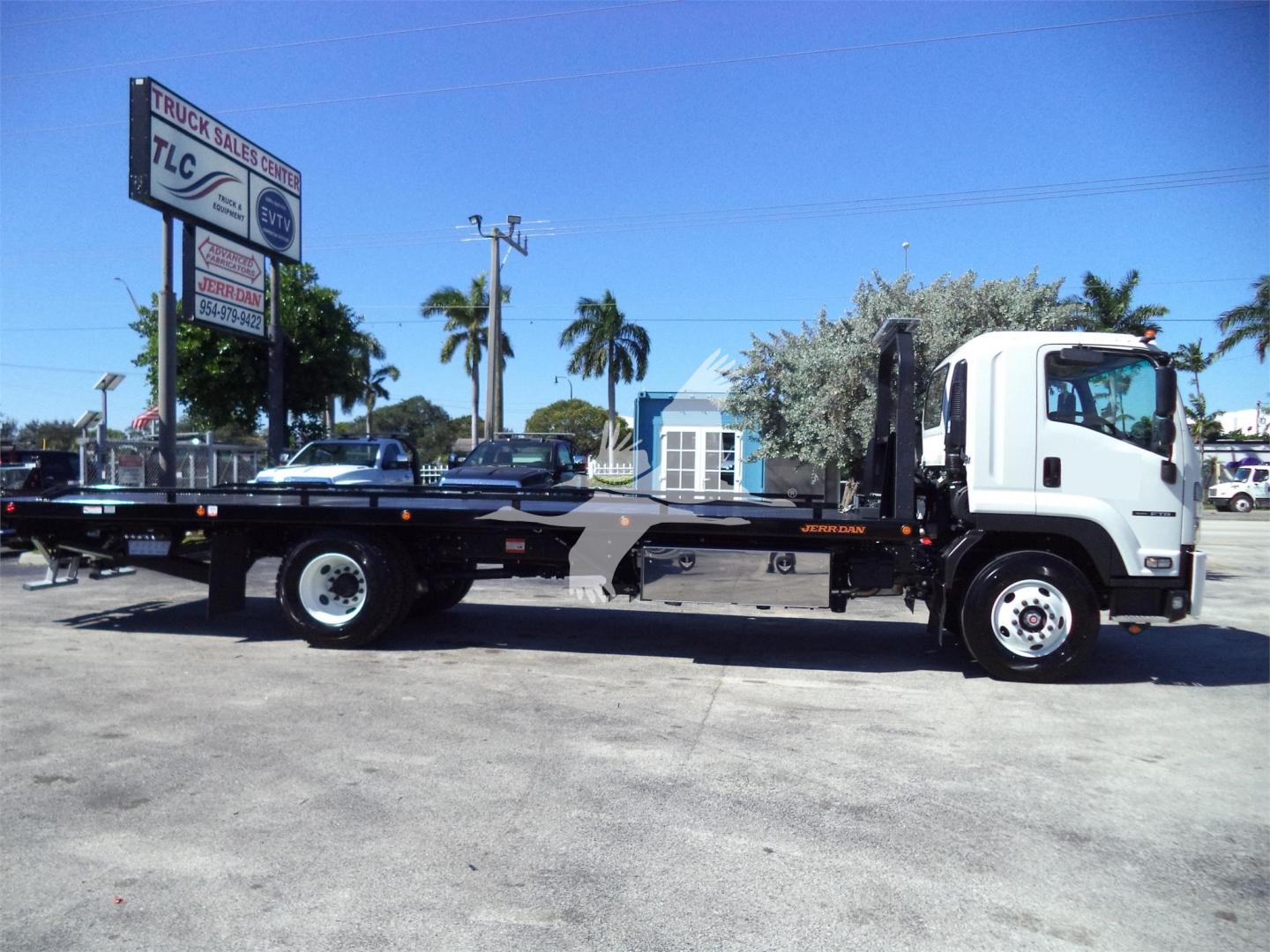 Isuzu FTR rollback truck in side view showing flatbed with black frame and white cab, dealership lot in background