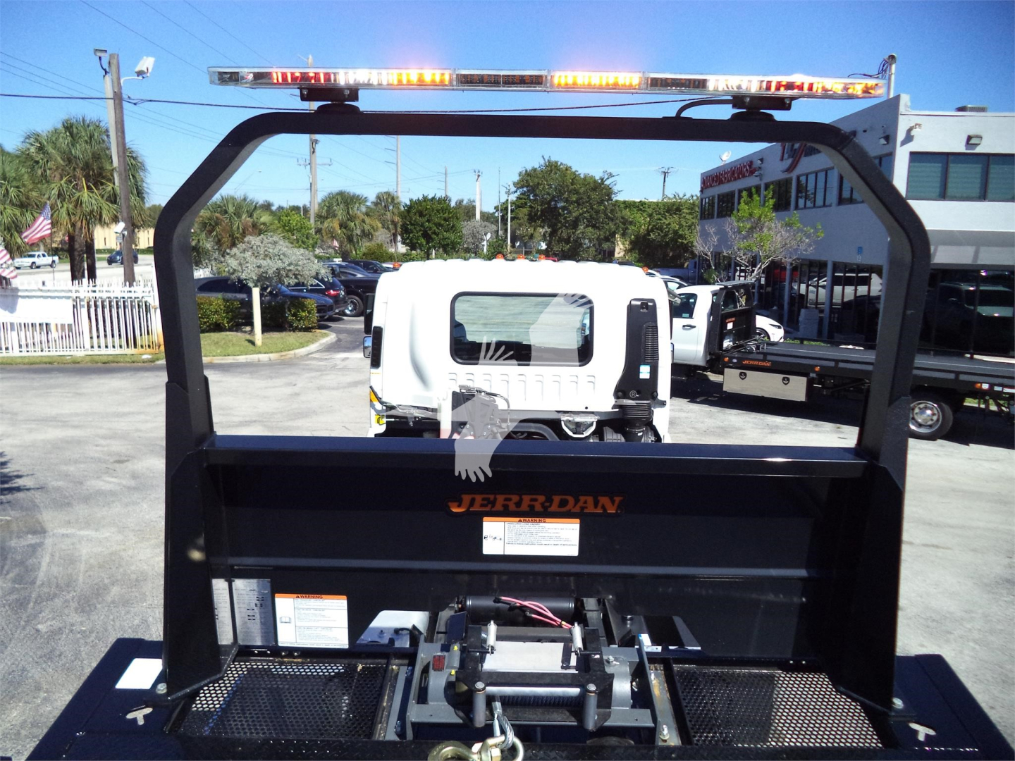 Isuzu rollback truck bed with JEER-DAN branding and safety rails, rear view showing hydraulic hitch and orange warning lights.