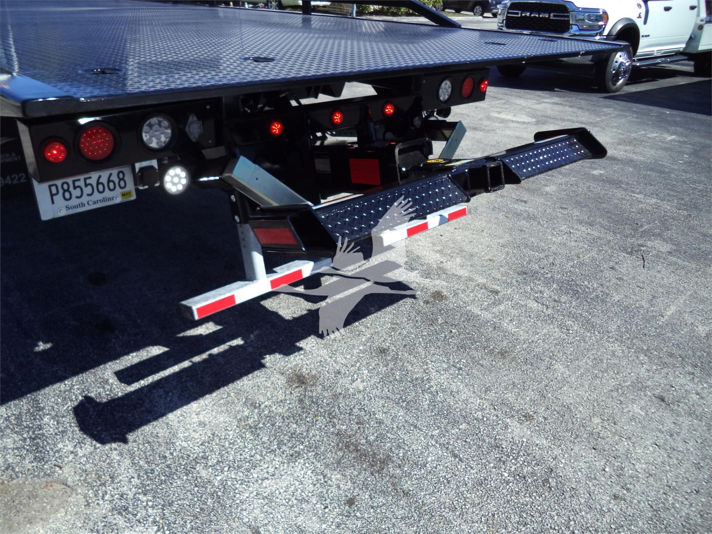 Isuzu FTR rollback truck rear with dual metal loading ramps and reflective safety tape; license plate visible.