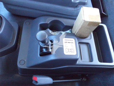 Isuzu FTR interior center console showing parking brake lever, gear shift shifter, cup holder, and a small cardboard box placed in the storage compartment.