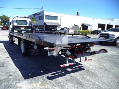 Isuzu rollback truck bed with flatbed and rear ramps in a dealership lot.