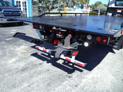 Isuzu FTR rollback bed showing hydraulic wheel lift and bumper accessories; flatbed with diamond plate surface and taillights visible.