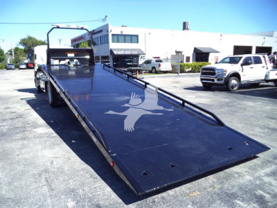 Isuzu FTR rollback truck with a lowered flatbed showing a white bird logo on the dark blue surface.