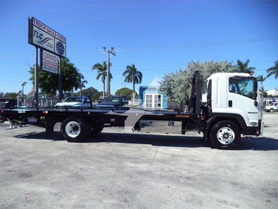 Isuzu FTR rollback truck in side view showing flatbed with black frame and white cab, dealership lot in background