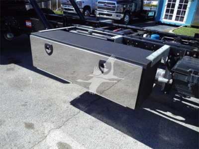 Isuzu FTR rollback truck chassis with a large rectangular aluminum toolbox mounted on the side, visible under clear sky.