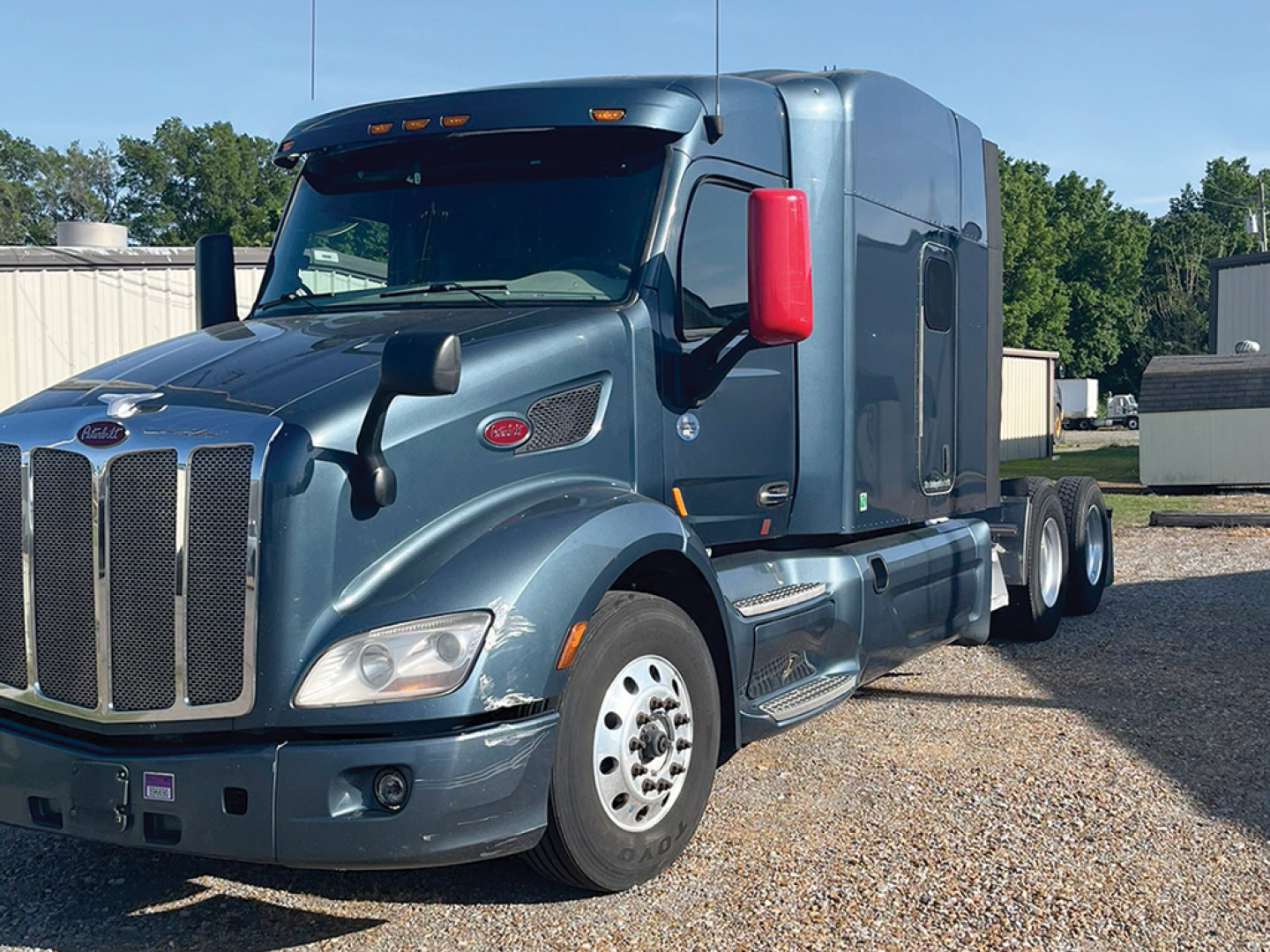 Peterbilt 579 UltraCab truck, side view, blue/gray, with red mirrors, triple rear axles, chrome grille and badge details visible.