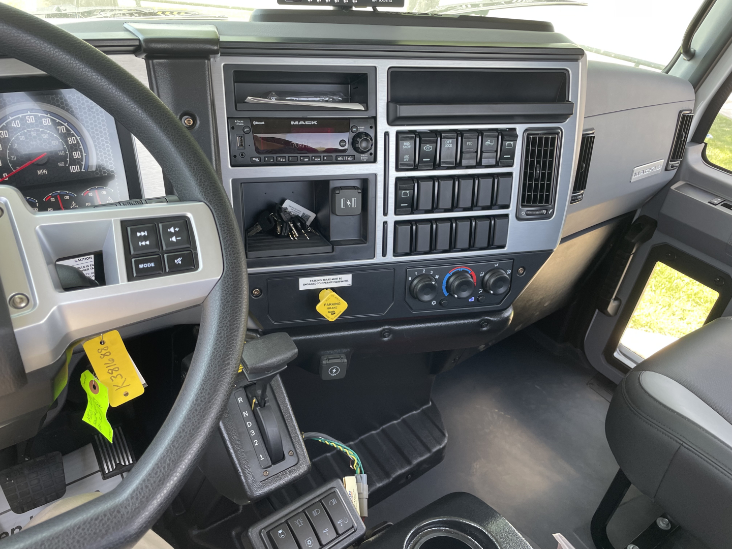 Cabin interior of a 2026 Mack MD6 showing steering wheel, instrument cluster, dashboard controls, radio, climate controls, and ashtray area.