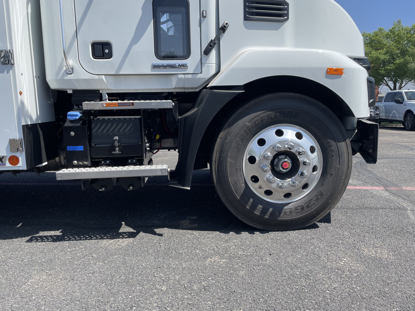Mack MD6 front wheel area showing tire, wheel, and steps with engine-compartment components visible on the left.