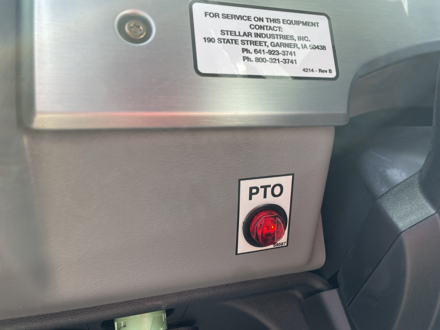 Label on equipment panel showing PTO button with red switch and service sticker; stainless steel surface and grey plastic panel.