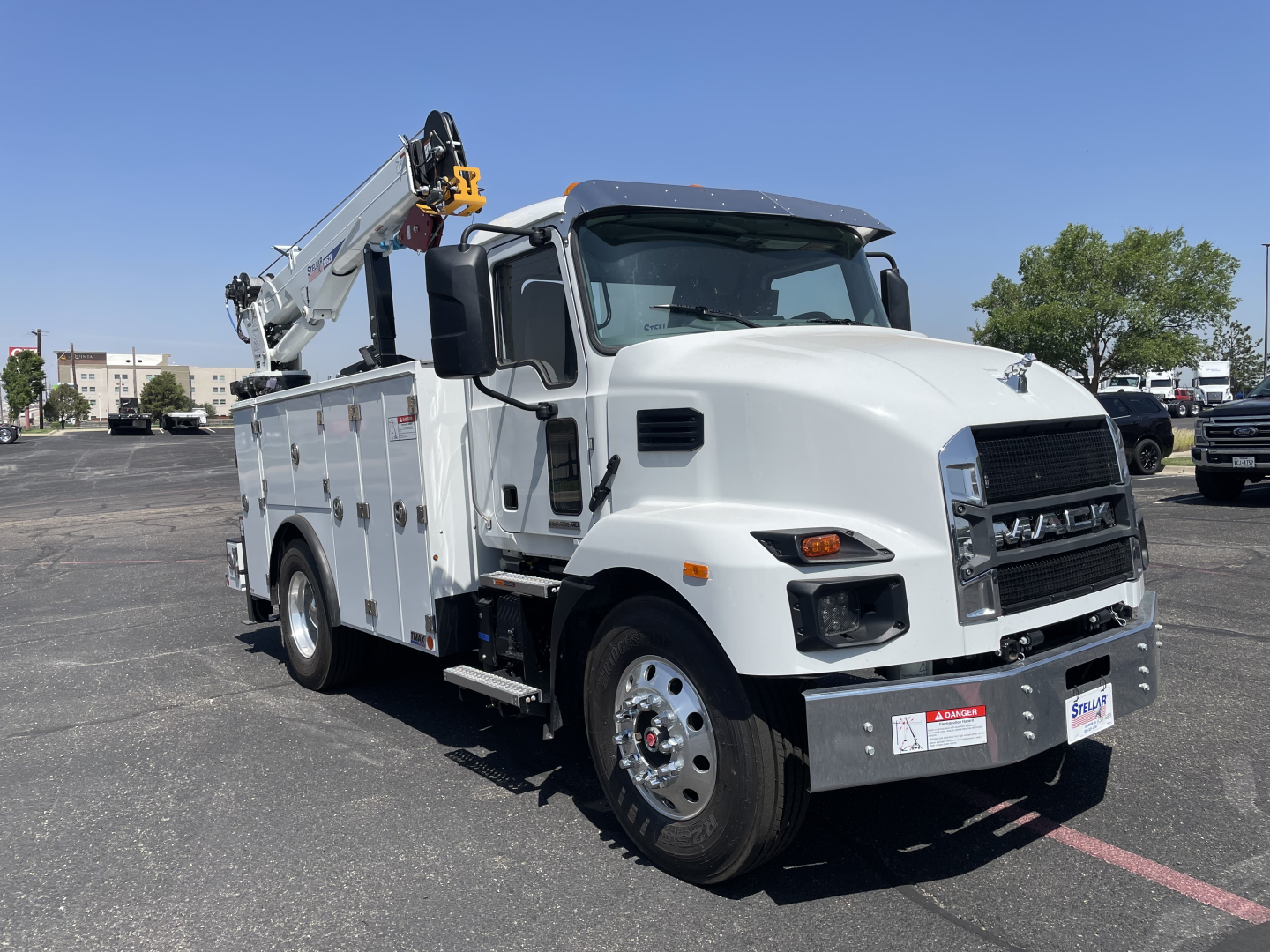 Front-right view of a white 2026 Mack MD6 service truck with utility compartments and a mounted crane; visible text includes MACK on grille and no other legible labels.