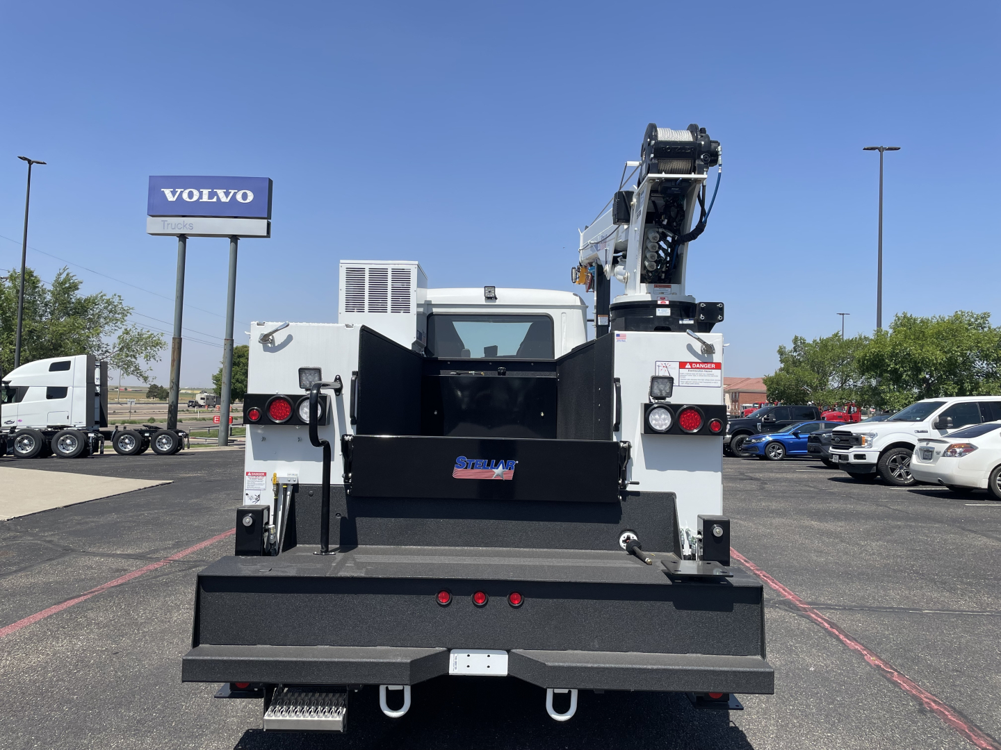 Back of a service/utility truck with a large flatbed and crane; rear doors open; tailgate and stows; text on small plate and branding on bumper.