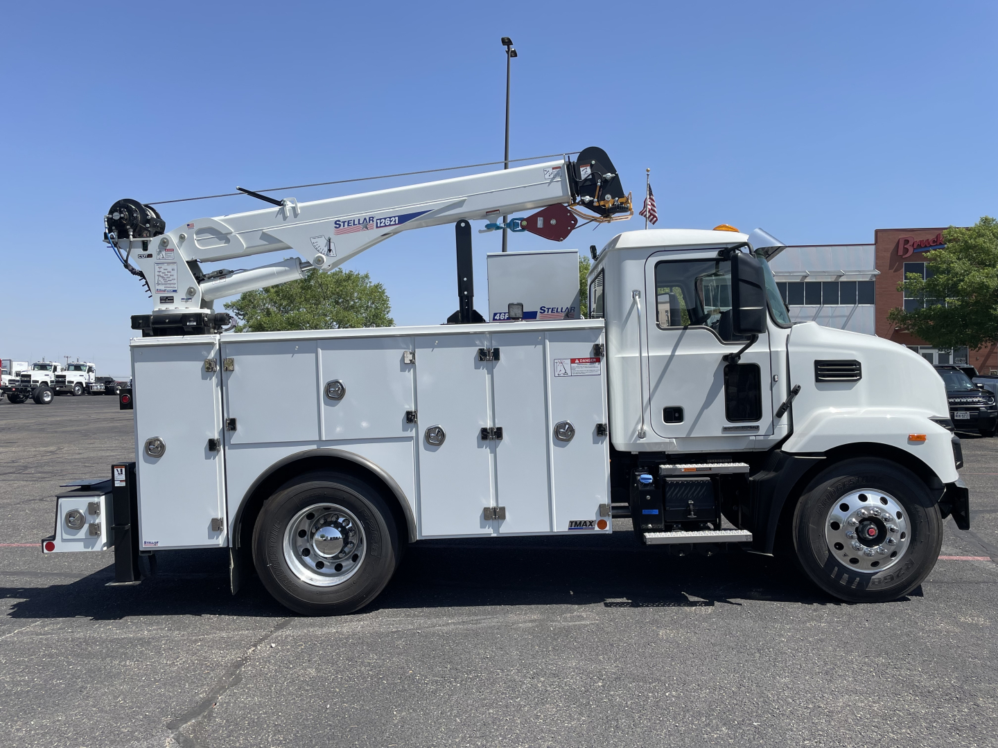 Service/utility truck with crane: white Mack MD6 utility body, mounted boom crane, compartments along side, cab and wheels visible.